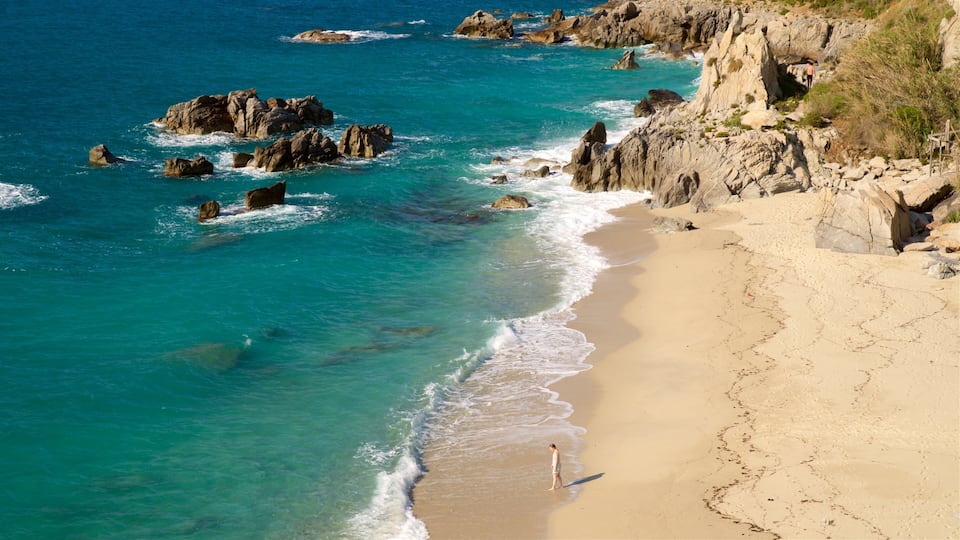A coastal landscape with clear turquoise waters, rocky outcrops, and a sandy beach.