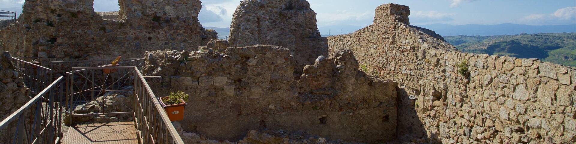 Ruinas de piedra antiguas con una pasarela metálica y un cielo azul despejado.