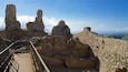 Ancient stone ruins with a metal walkway and a clear blue sky.