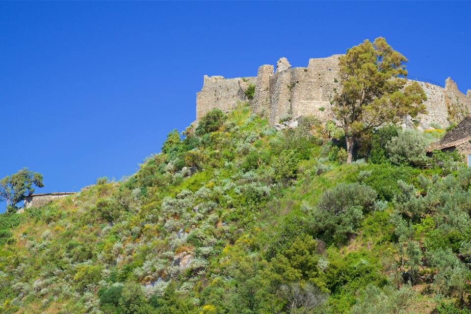 A historic stone castle atop a hill with lush greenery and a clear blue sky.