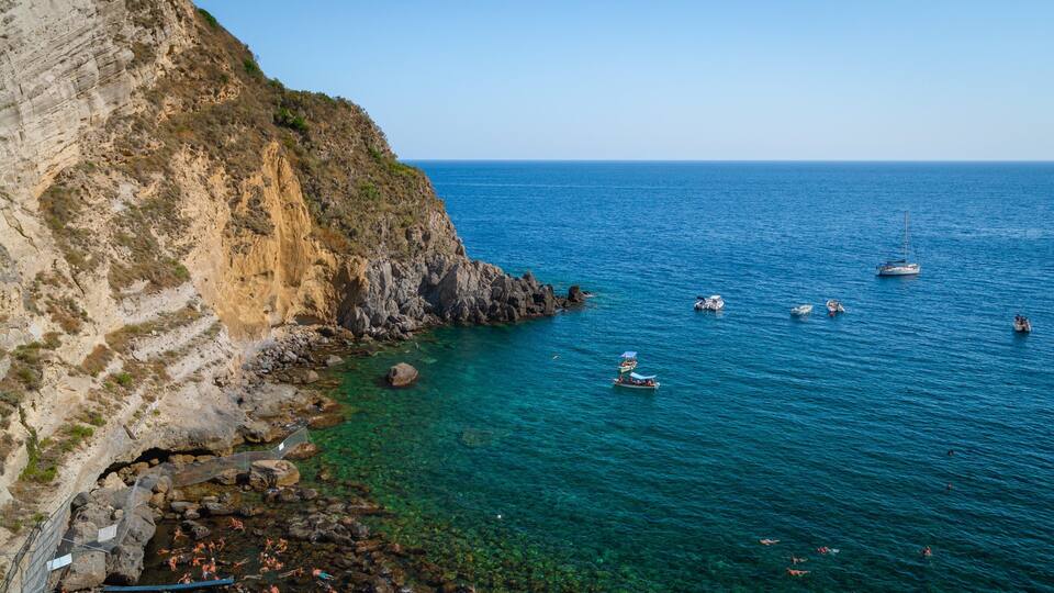A coastal landscape with cliffs, clear blue sea, and several boats.