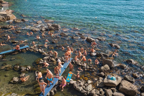 Eine Gruppe von Menschen schwimmt und entspannt sich in einer felsigen Bucht mit klarem Wasser.