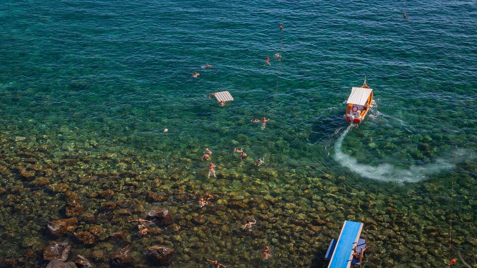 A clear blue sea with people swimming and a boat anchored near the shore.