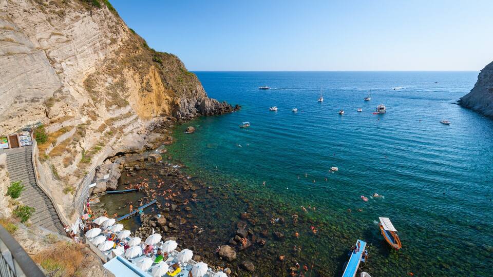 A coastal area with clear waters, rocky cliffs, and a pier with boats.