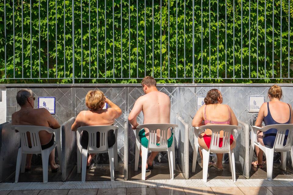 Persone sedute su sedie di plastica vicino a un muro con vegetazione verde.