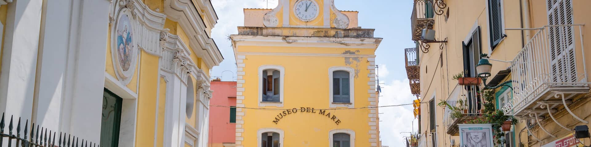 Une rue bordée d’un immeuble jaune sur lequel on peut lire l’inscription « Museo del Mare » et d’un beffroi.