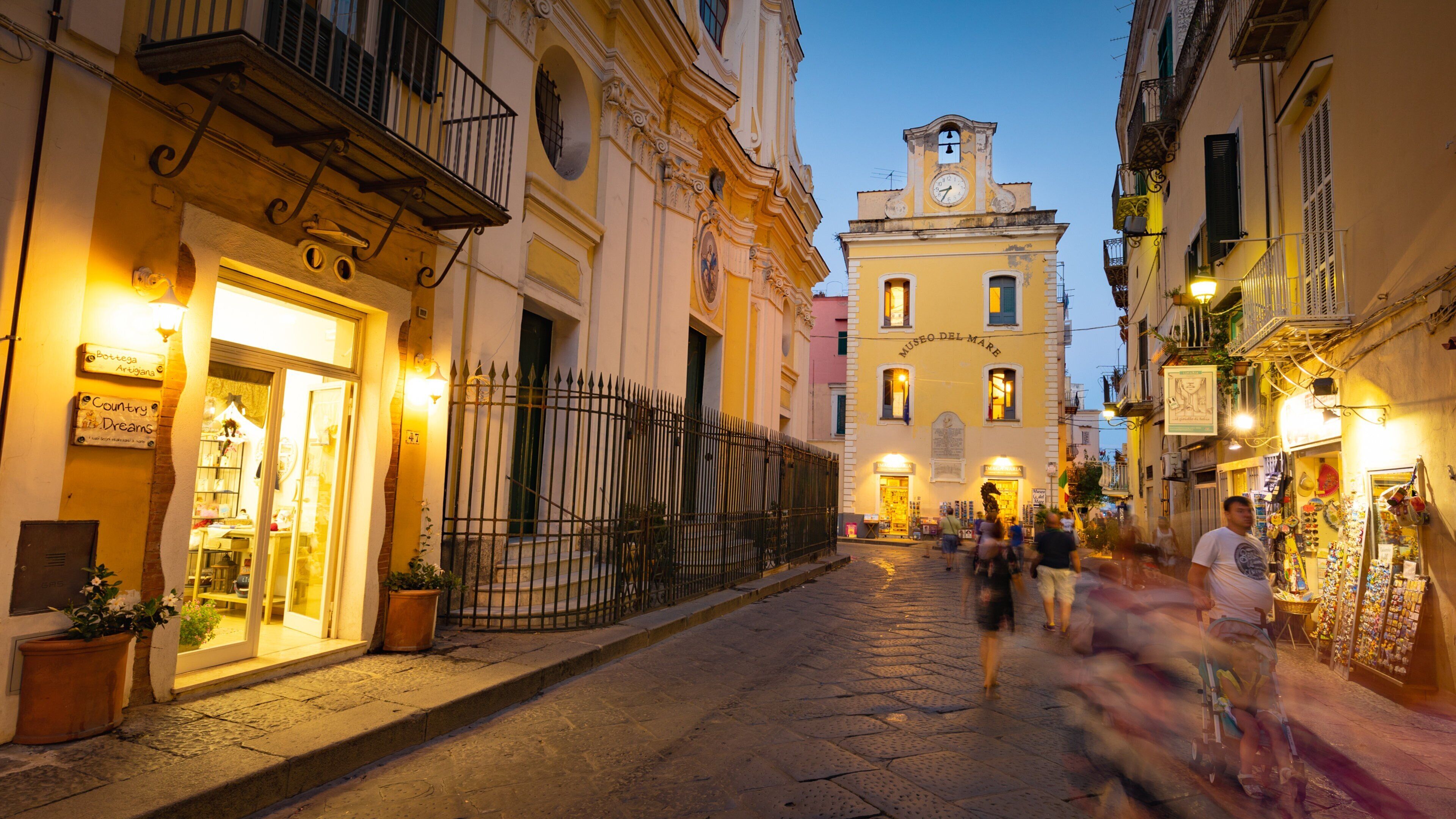 A cobblestone street with historic buildings, a clock tower, and people walking.
