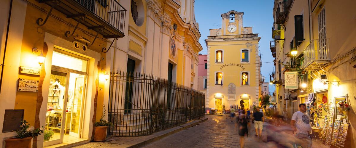 A cobblestone street with historic buildings, a clock tower, and people walking.