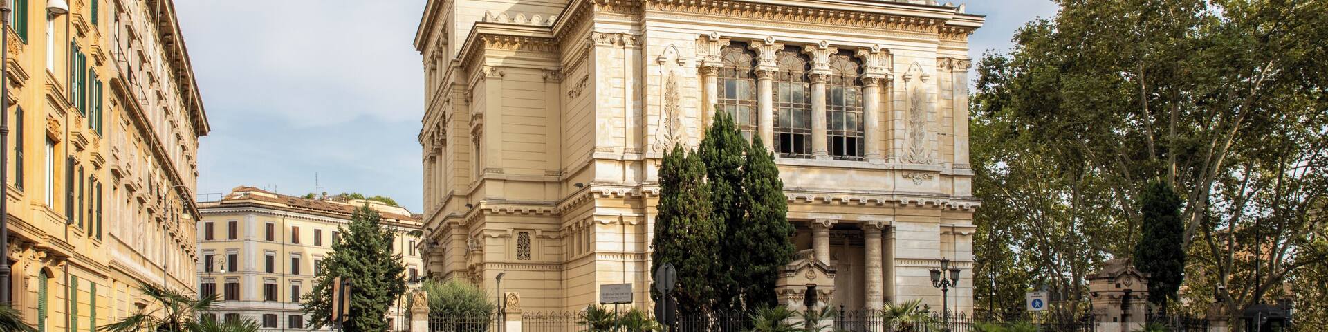 Un edificio histórico con una cúpula y columnas, rodeado de una plaza adoquinada y árboles.