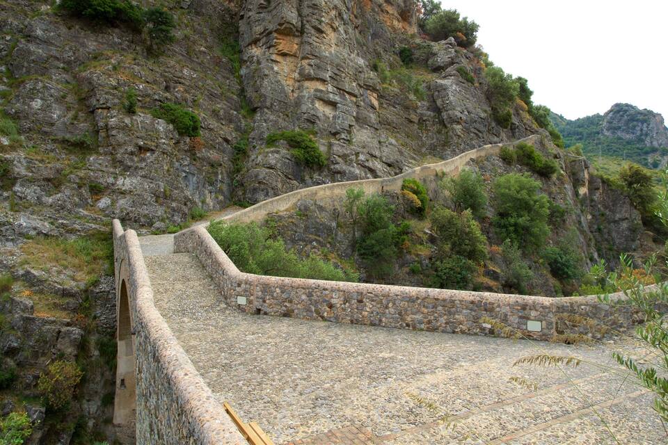 Un puente de piedra con un precipicio pronunciado en un lado, rodeado de terreno rocoso y vegetación escasa.