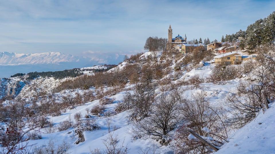 A snow-covered mountain landscape with a church and residential buildings on a hillside.