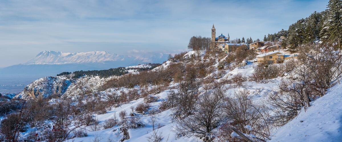 A snow-covered mountain landscape with a church and residential buildings on a hillside.