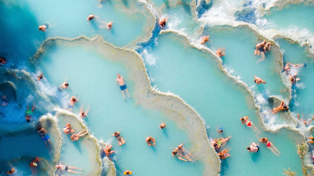 Aerial view of turquoise ocean with sunbathers at Saturnia spa, Cascate del Mulino, Hot Spring, Manciano, Italy.