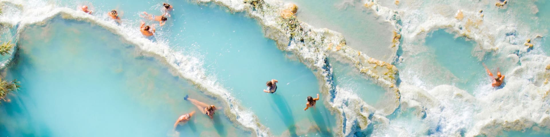Aerial view of turquoise ocean with sunbathers at Saturnia spa, Cascate del Mulino, Hot Spring, Manciano, Italy.