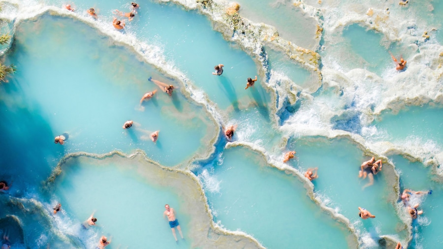 Aerial view of turquoise ocean with sunbathers at Saturnia spa, Cascate del Mulino, Hot Spring, Manciano, Italy.