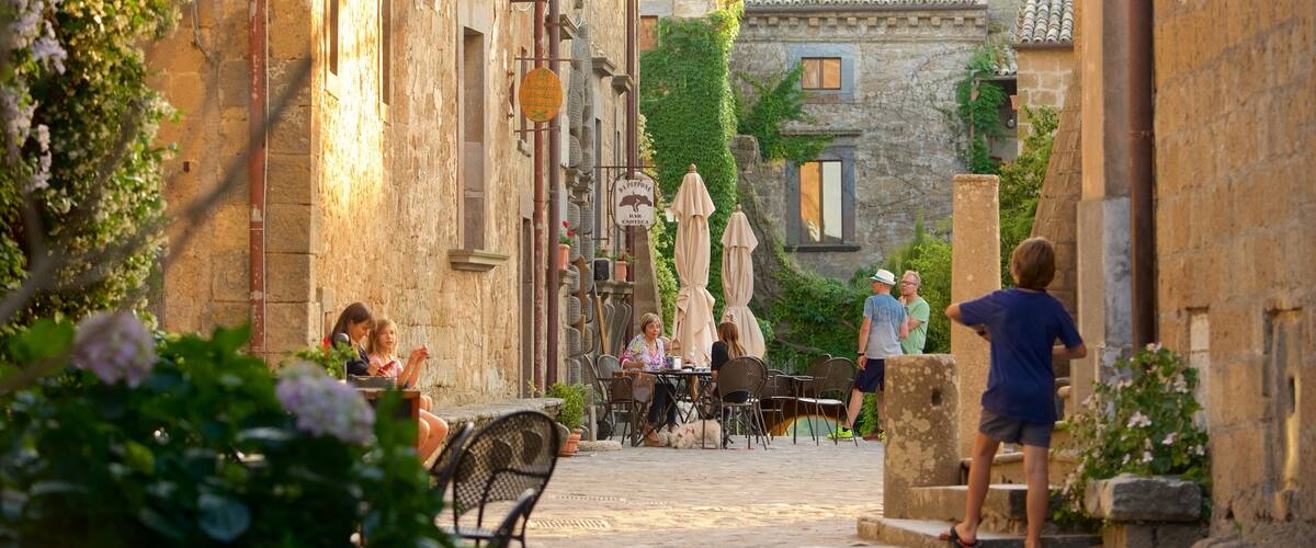 A cobblestone street with stone buildings, outdoor seating, and greenery.