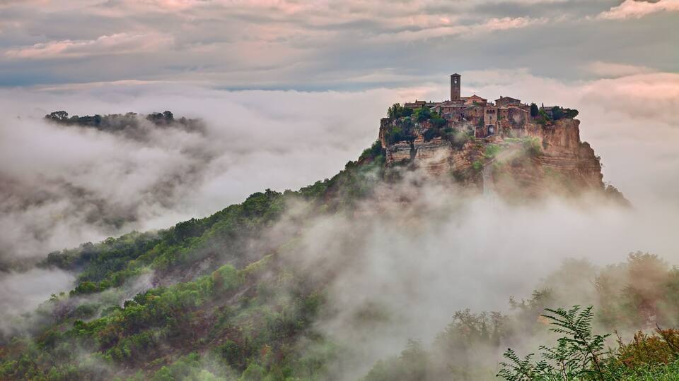 A historic castle perched atop a cliff, surrounded by lush greenery and enveloped in mist.
