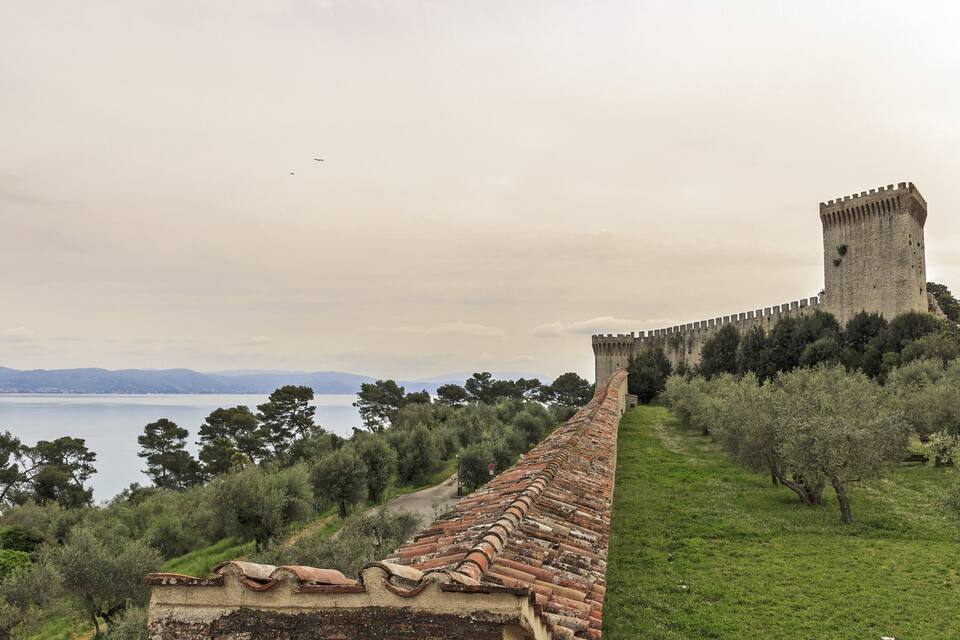 A historic stone wall with a tower overlooking a body of water and distant mountains.