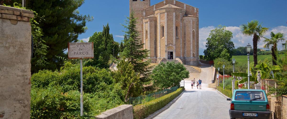 A historic church with a bell tower, surrounded by lush greenery and a paved road.