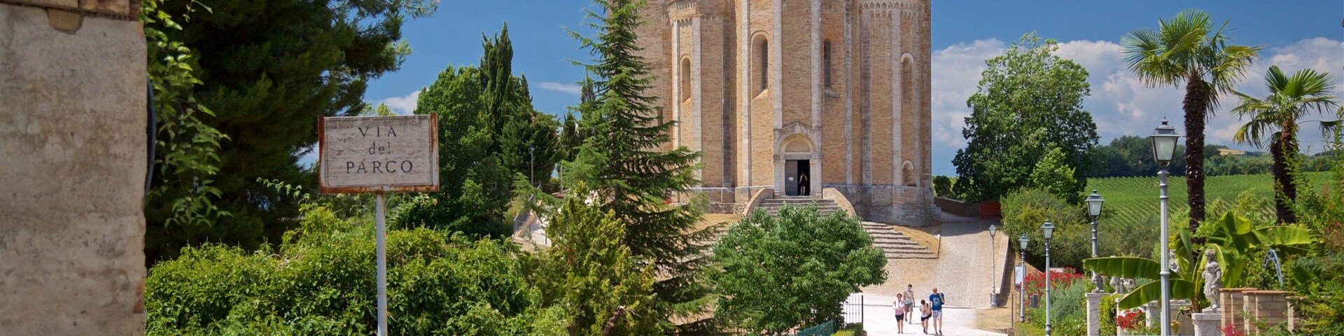 A historic church with a bell tower, surrounded by lush greenery and a paved road.