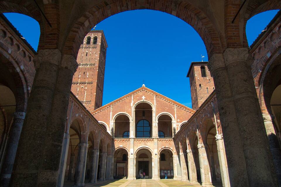 A historic building with a central arched walkway, two towers, and a clear blue sky.
