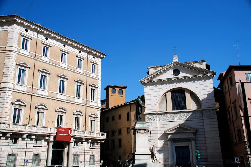 A historic building with classical architecture, a prominent statue, and a clear blue sky.