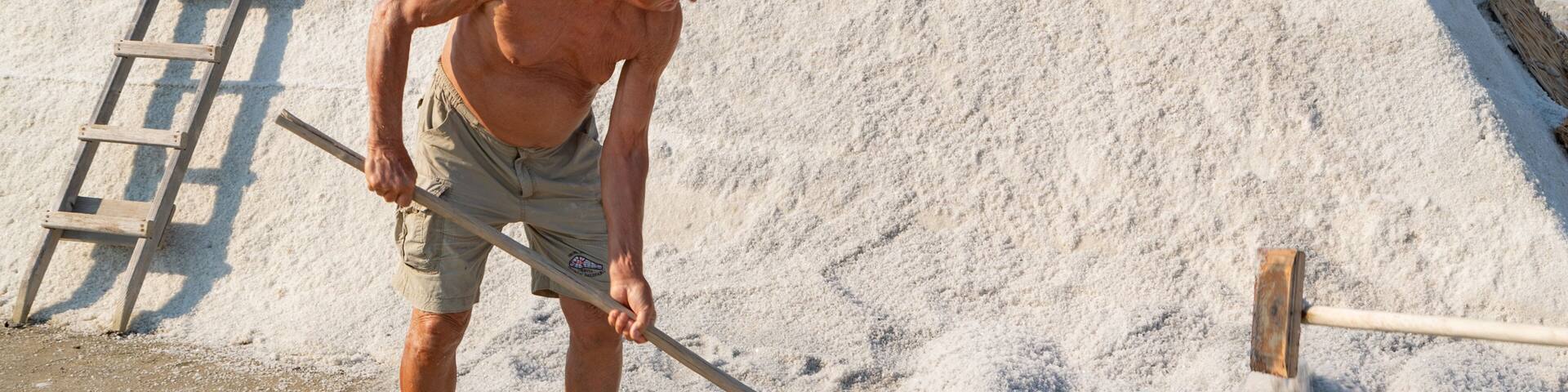 A man shoveling sand with a shovel and a wooden ladder beside him.