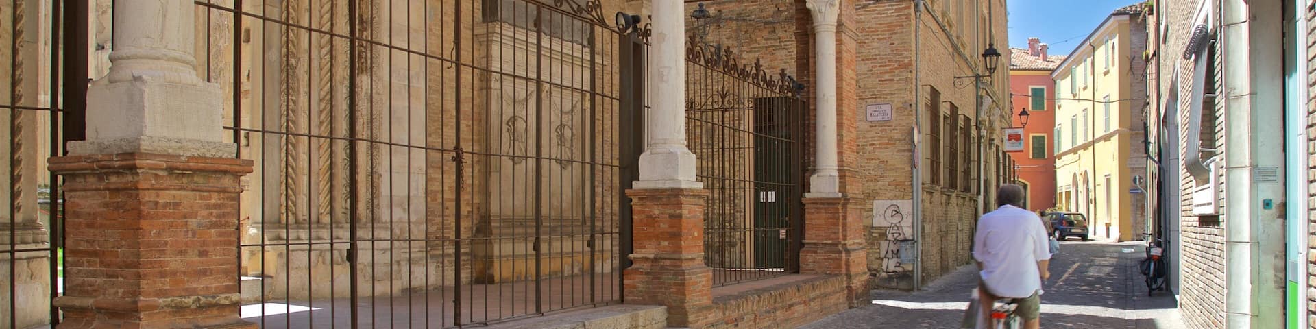 A cobblestone street with a man riding a bicycle, historic buildings with brick facades, and ornate metal gates.