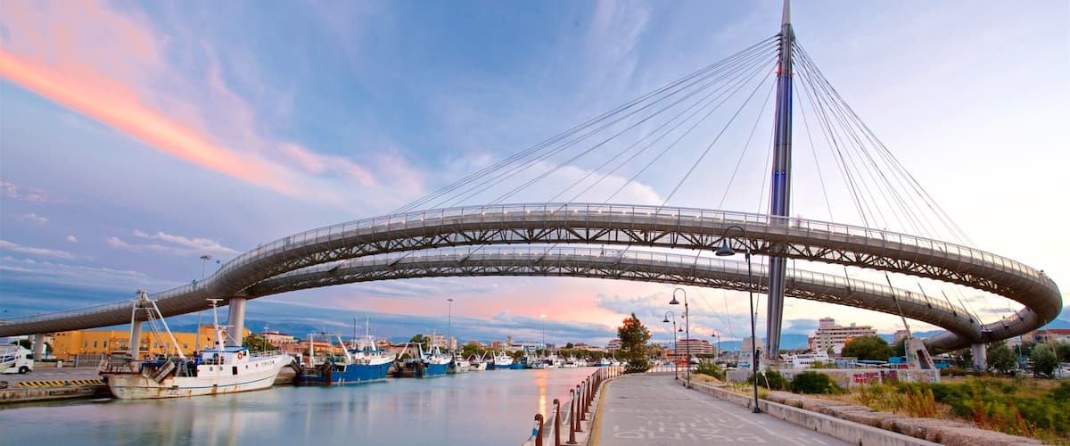 A large, modern bridge spanning a body of water, with boats docked nearby and a cityscape in the background.