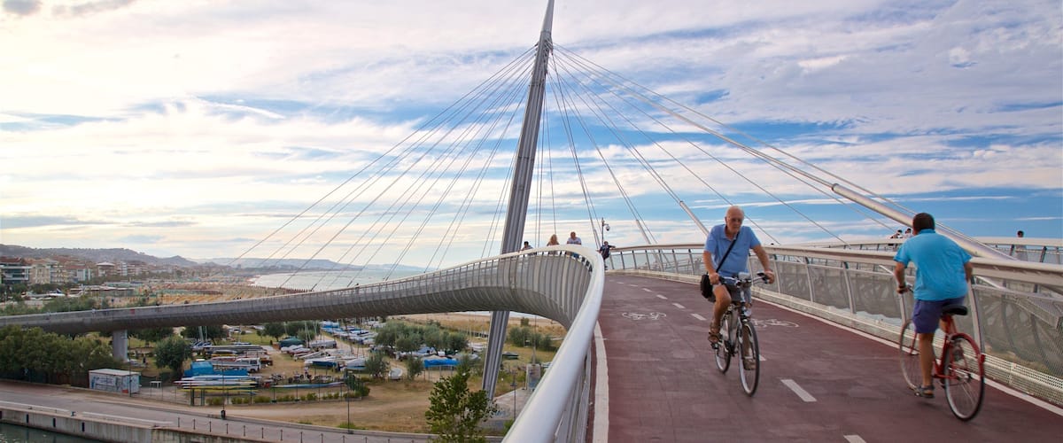 Un moderno puente atirantado con un paseo curvo distintivo, ciclistas en la vía y un río abajo.