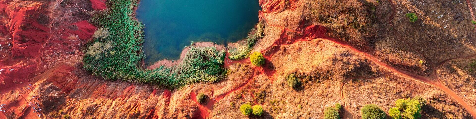 Paisaje rojizo con un lago azul en el centro, rodeado de vegetación verde.