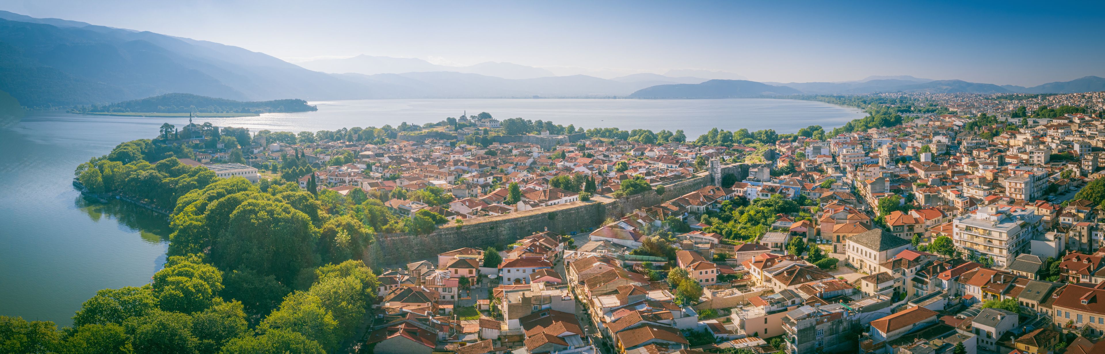Un paysage urbain côtier caractérisé par une imposante fortification, une vaste étendue d’eau et un arrière-plan montagneux.