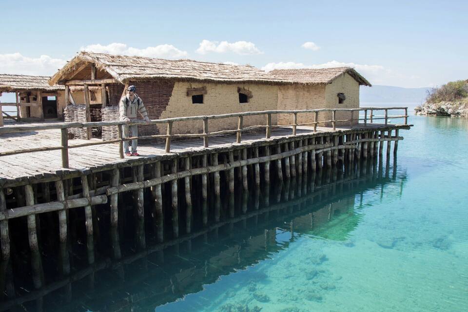 A wooden pier extending into clear blue water with traditional huts at the end.