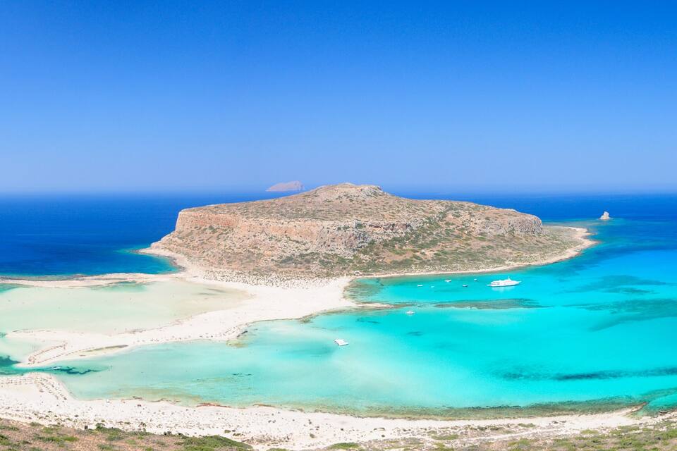 A coastal landscape with a prominent rocky island, clear turquoise waters, and a sandy beach.