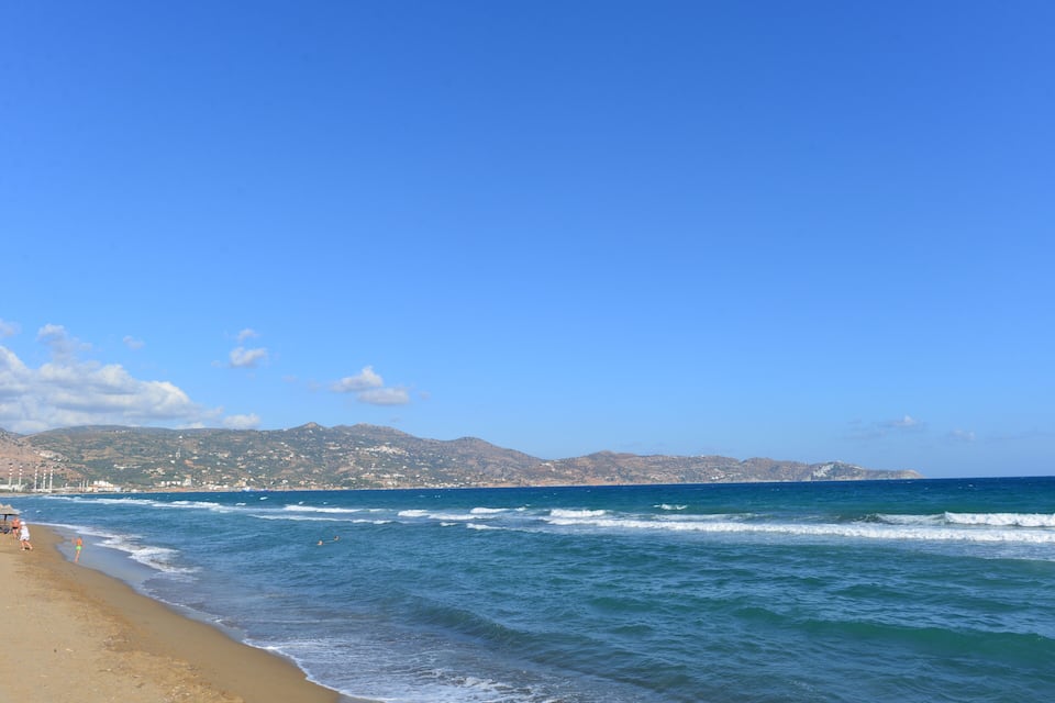 A beach with waves, a clear sky, and distant hills.