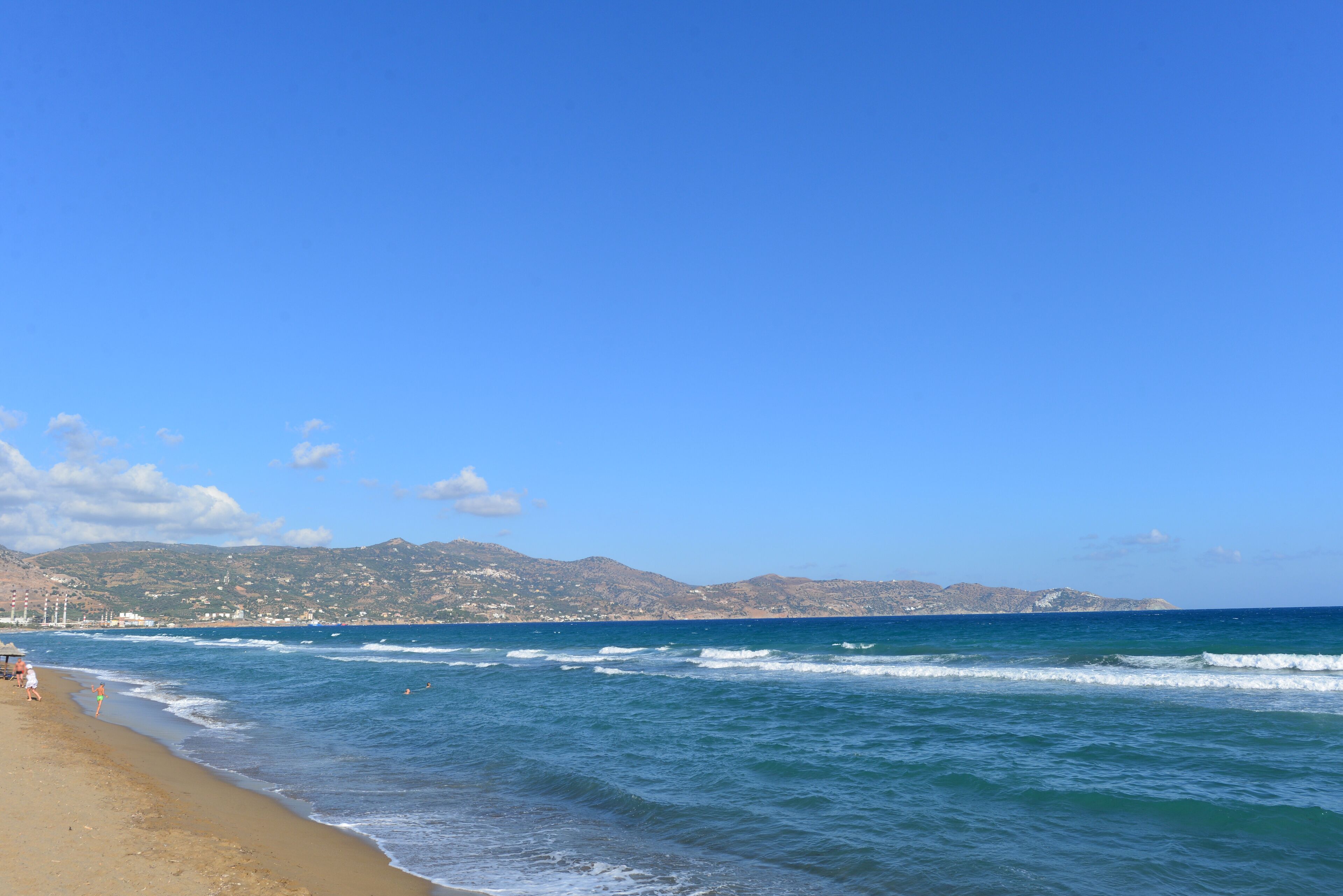 A beach with waves, a clear sky, and distant hills.