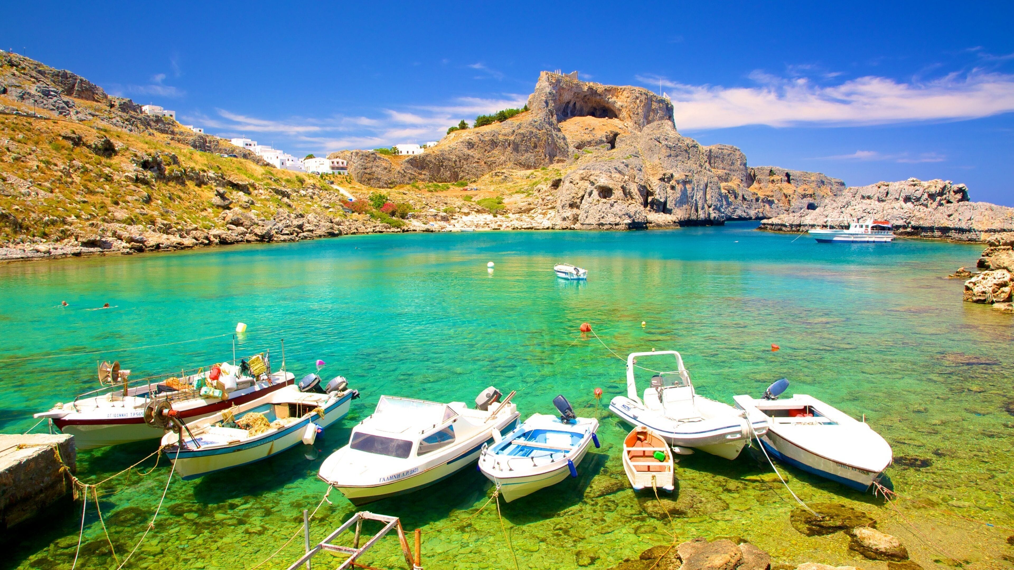 A coastal scene with clear turquoise water, rocky cliffs, and several anchored boats.