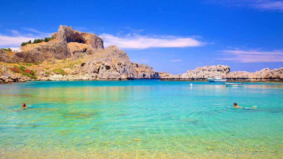 A clear turquoise sea with rocky cliffs and a castle.