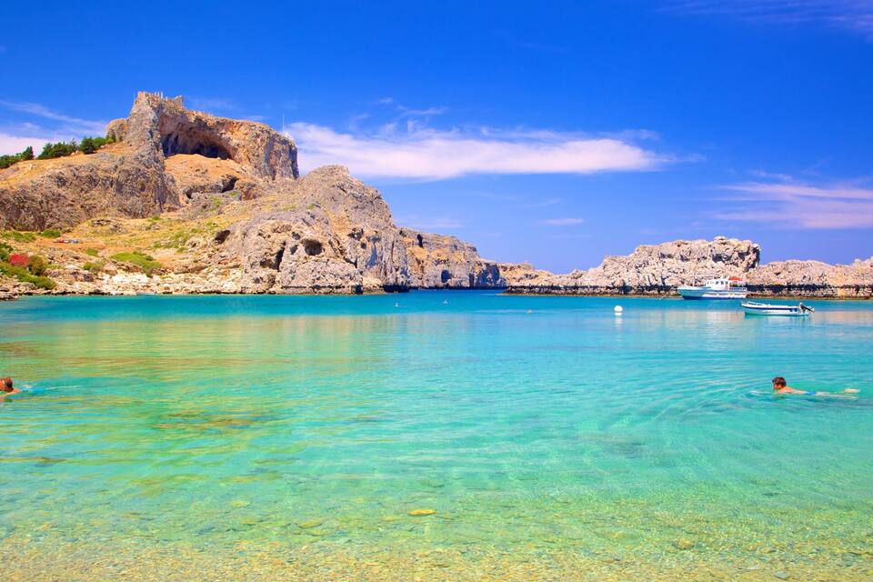 A clear turquoise sea with rocky cliffs and a castle.