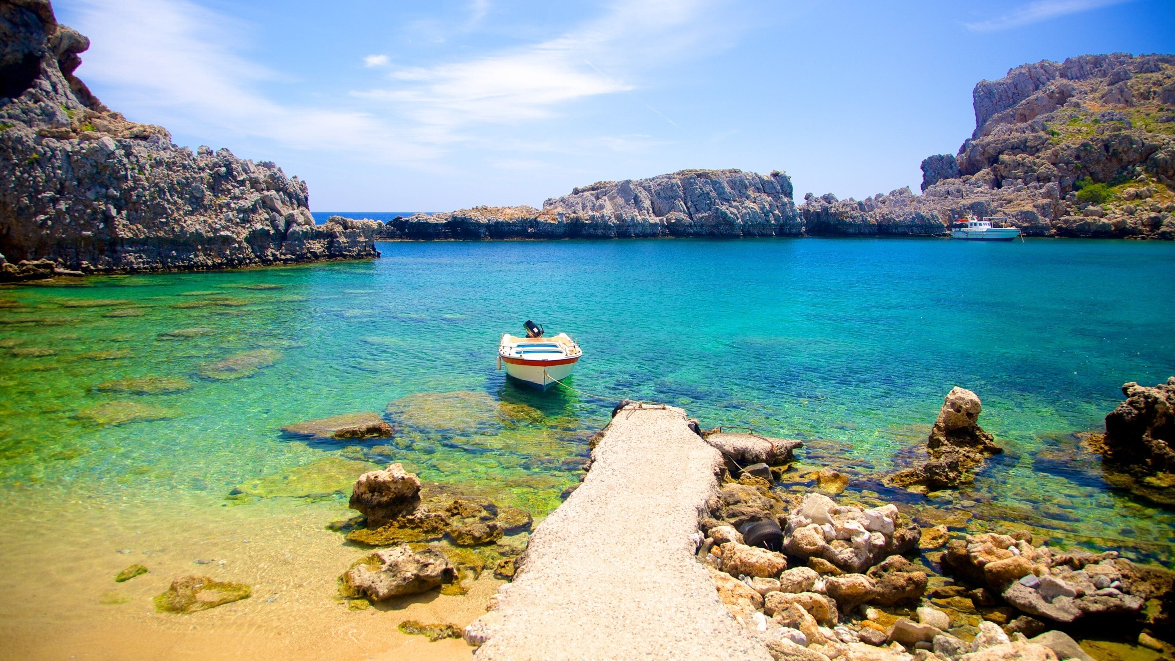 A boat anchored in a clear turquoise sea with rocky cliffs.