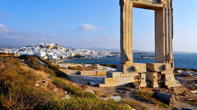 Ancient ruins with a stone archway, a coastal town in the background, and a clear blue sky.