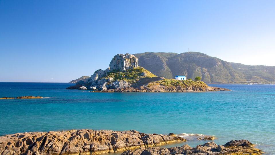 A rocky coastline with a small island featuring a white building with a blue roof.