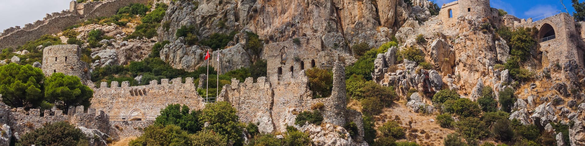 A rugged mountain with ancient ruins, including a castle and a tower, surrounded by rocky terrain and sparse vegetation.