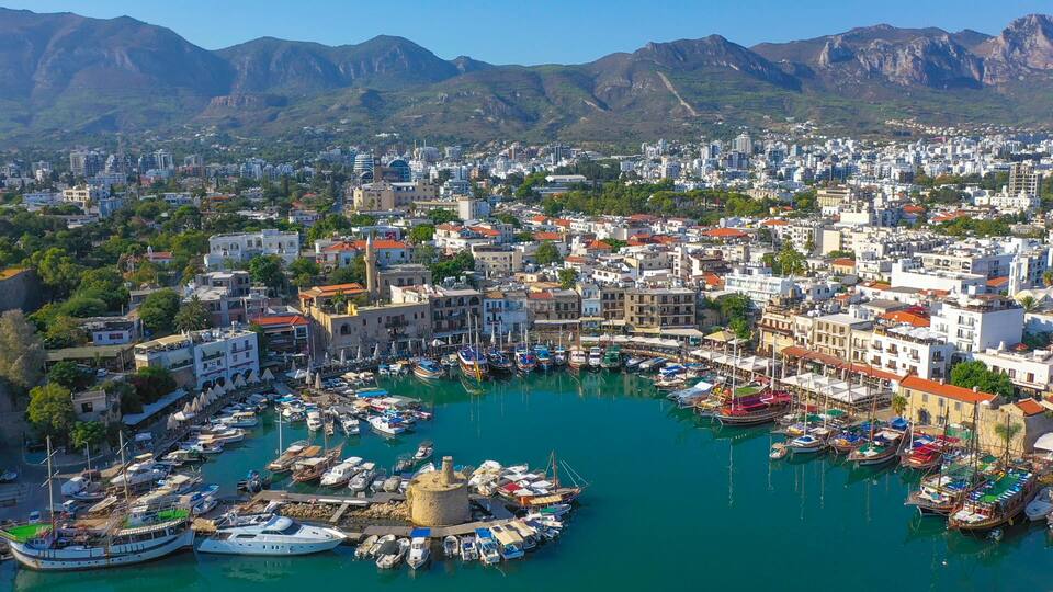 A coastal town with a marina filled with boats, surrounded by mountains and dense urban buildings.