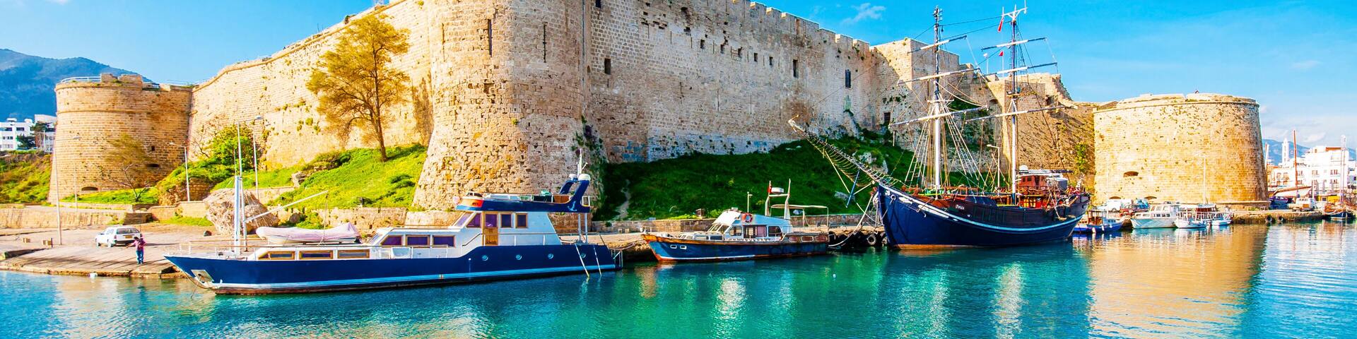 Un castillo histórico junto a un mar azul cristalino, con barcos amarrados al frente.