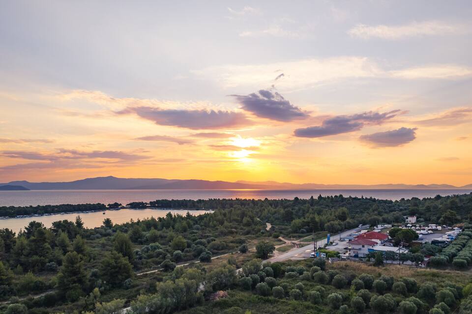 Un paysage côtier avec un coucher de soleil, une étendue d’eau et un parking bordé de bâtiments.