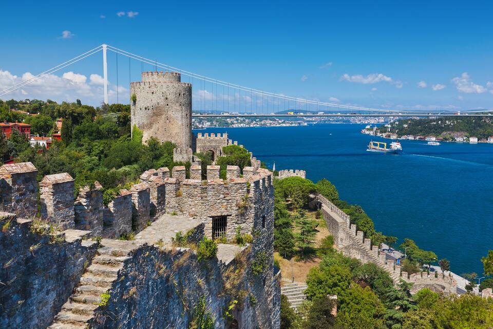 A historic stone fortress overlooking a body of water with a modern bridge in the background.