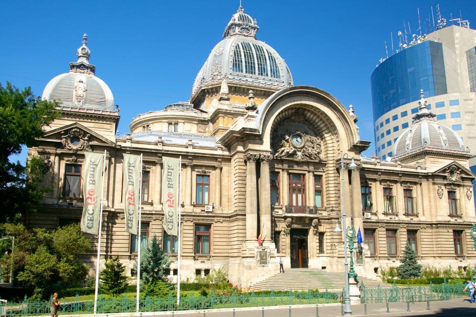 Un edificio histórico con arquitectura ornamentada, que incluye una gran cúpula y columnas, y un rascacielos moderno al fondo.
