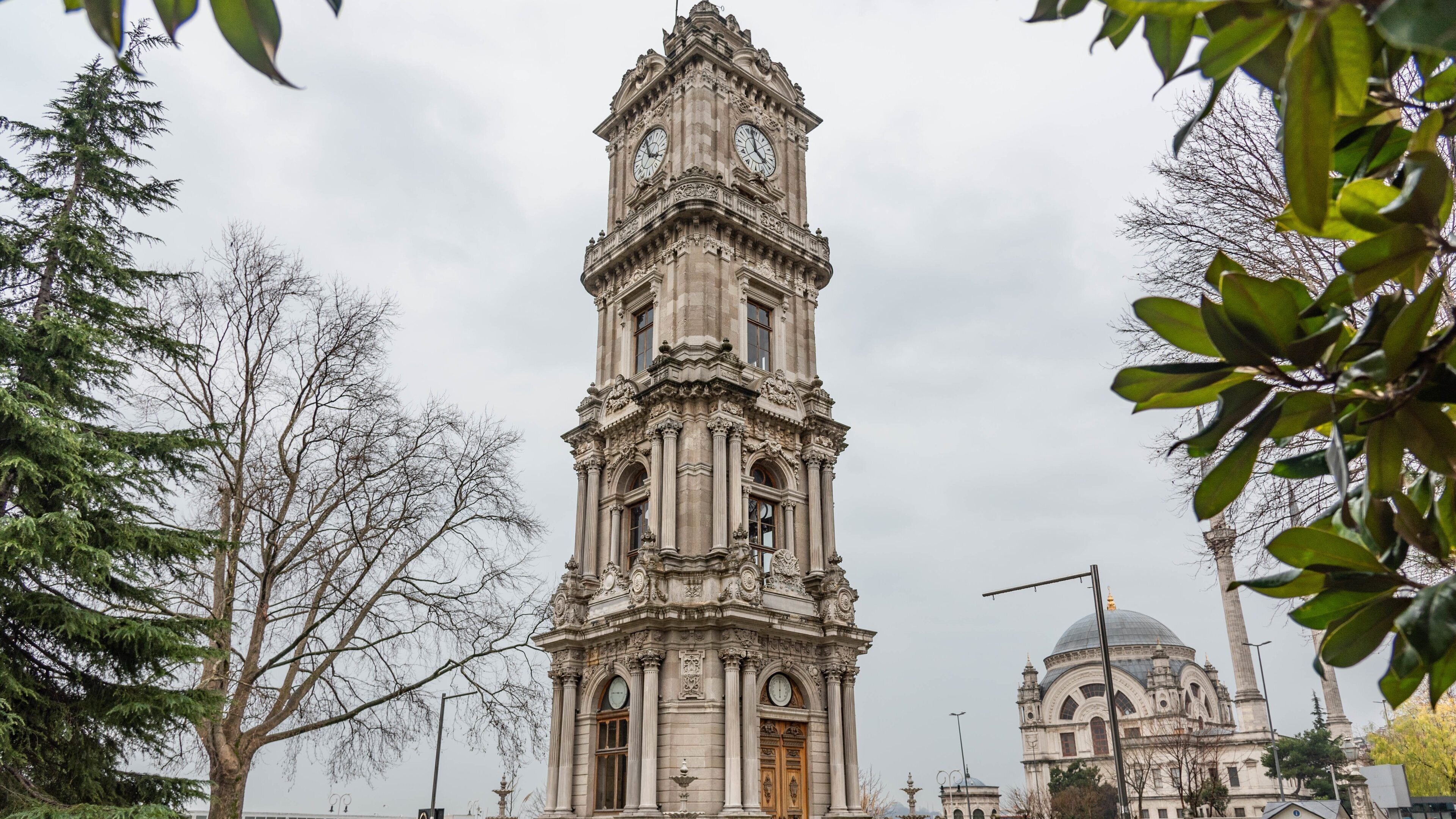 A historic clock tower with intricate carvings and a dome in the background.