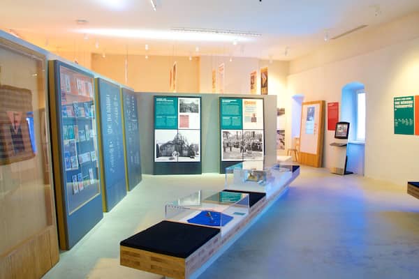 Exposição interna com vitrines de vidro, cartazes informativos e um banco de madeira.